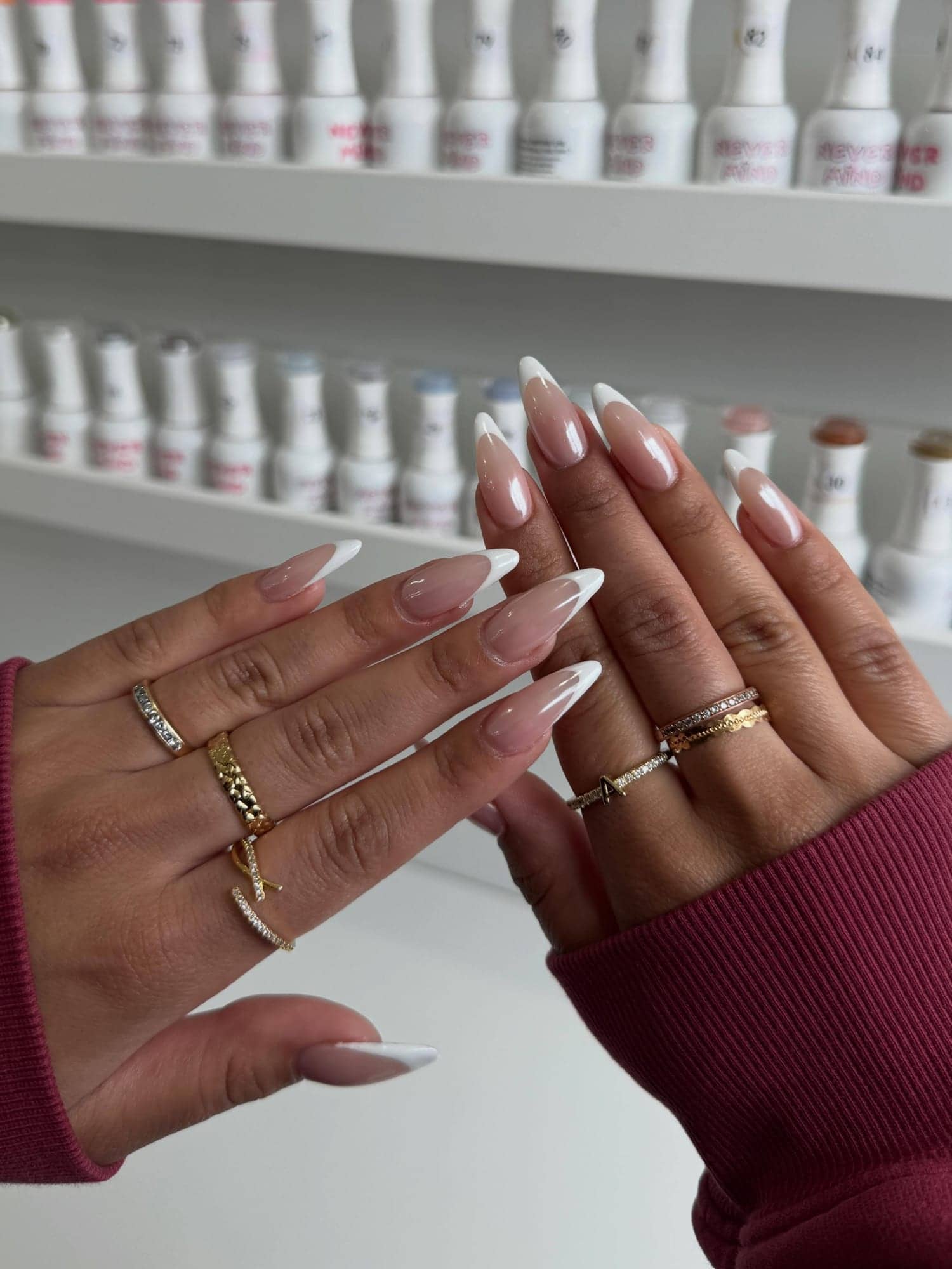 French-tip nails held up in front of the polish wall at Em Nail Studio